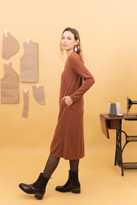 Vista lateral del vestido midi Spirit en color Roiboos, con la mano en el bolsillo y botas negras